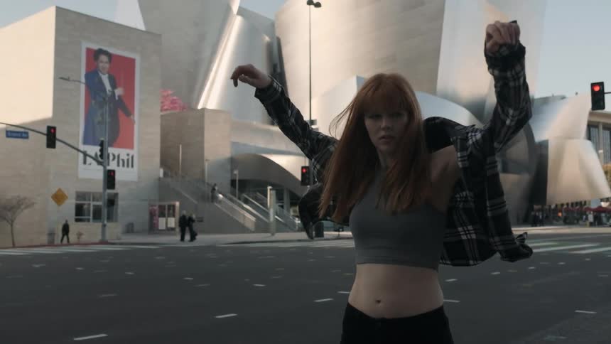 A red haired woman puts on a flannel shirt outside