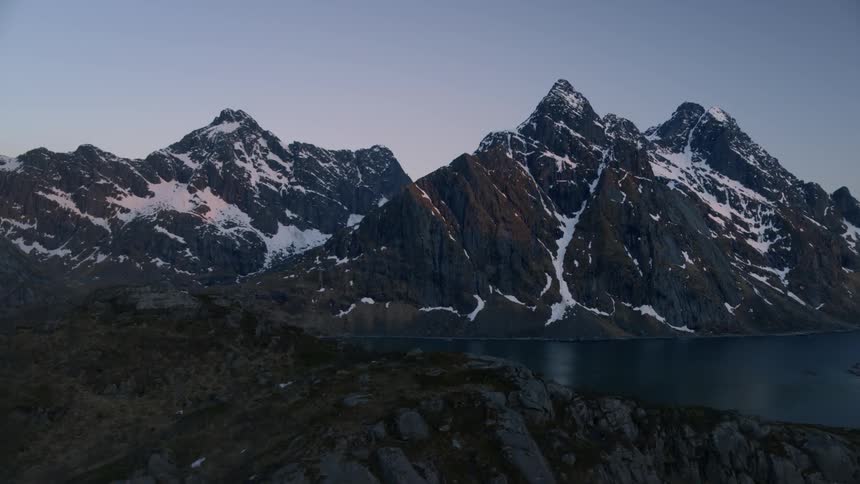 Snow covered mountains rise above a shoreline at dusk
