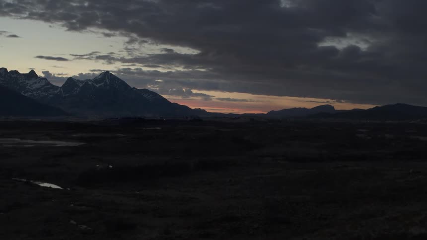Dark clouds hang over an open field by mountains