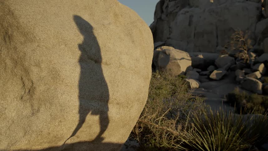 A woman's shadow runs near a large rock