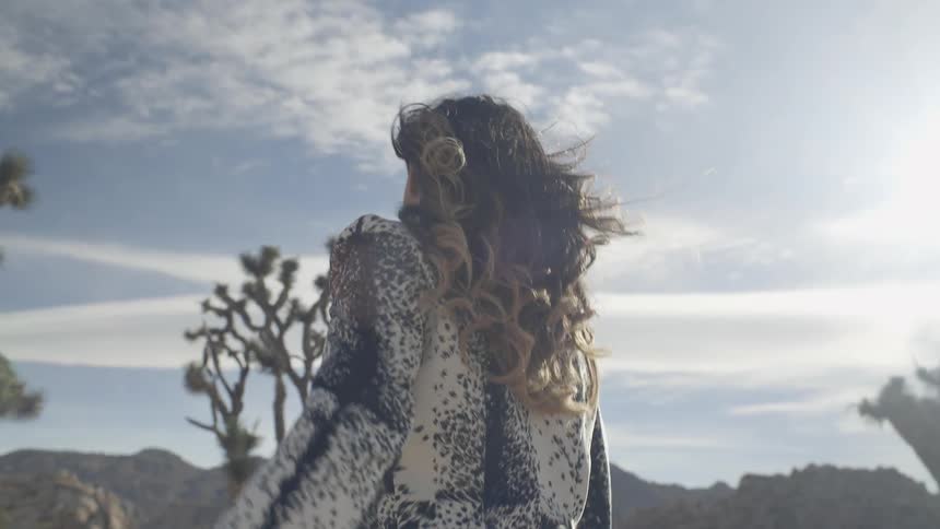 A woman looks over her shoulder and raises her arm as she walks in the desert