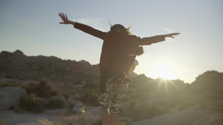 A woman holds her arms to the breeze as she walks in a desert