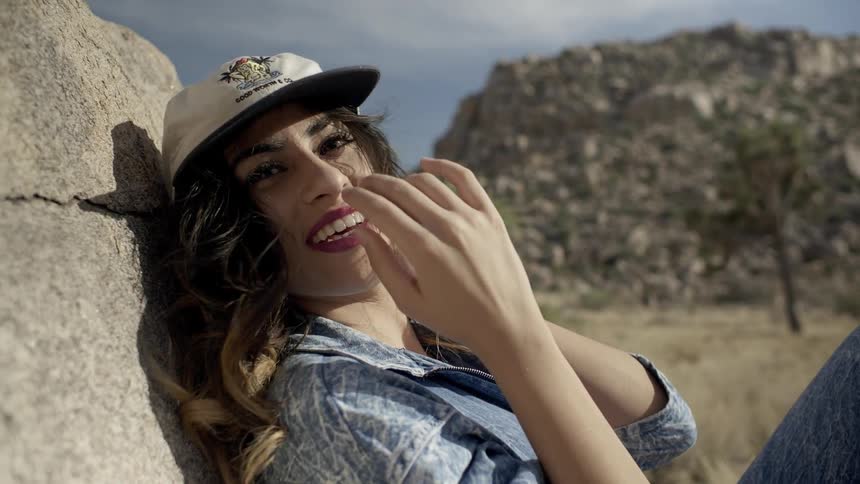 A woman wearing a hat smiles laying against a rock