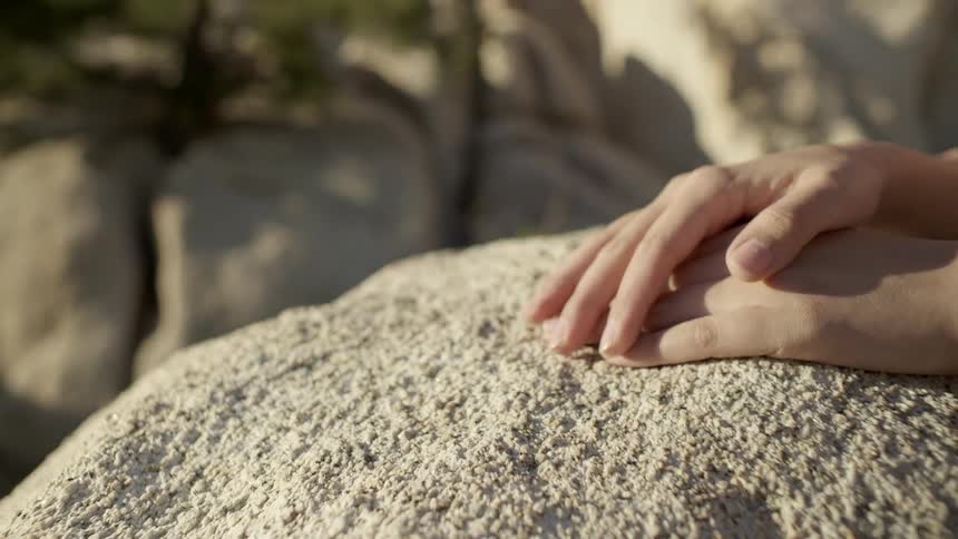 A woman runs her hands along the surface of a boulder