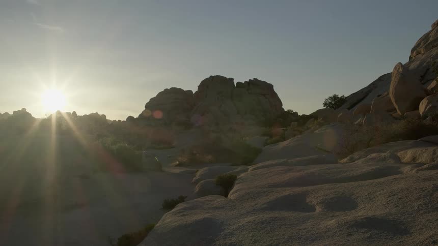 The sun casts rays and shadows over a desert landscape at dawn