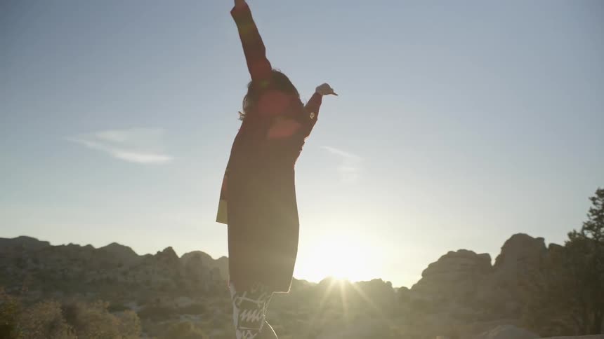 A woman raises her arms above her head and sways as she stands in the desert