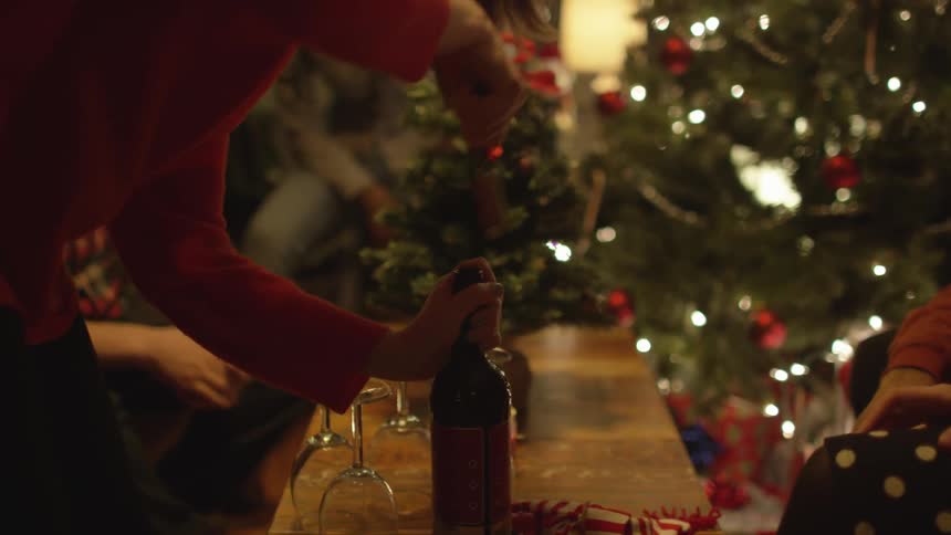 A woman opens a bottle of wine on in front of a christmas tree