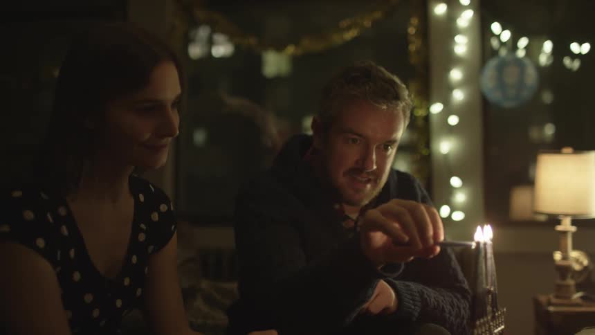 A man puts a candle into a bottle while a woman watches