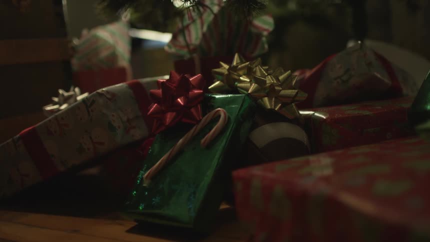 A person places a christmas present with other presents