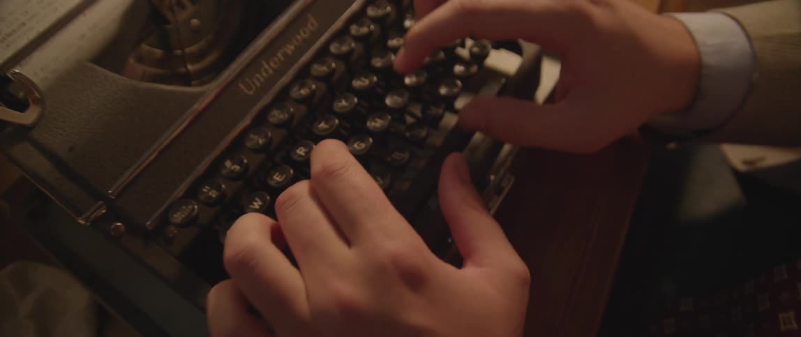 A man in  suit types on an old fashioned typewriter