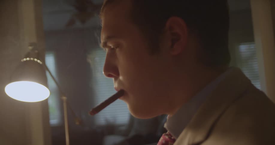 A young man smokes a cigar while typing on a desktop typewriter