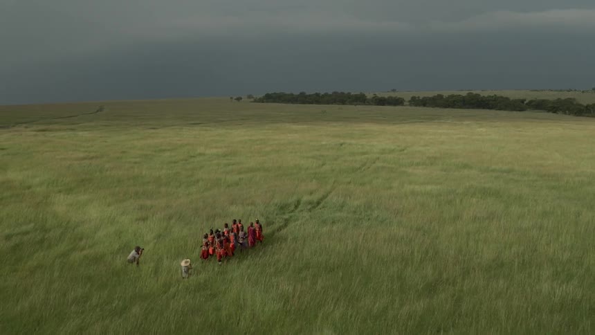 A group of maasai dance and sing as two photographers film them