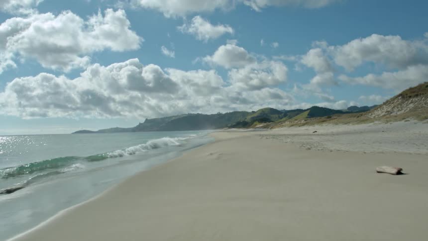 A beach with waves coming in and mountains and clouds in the background