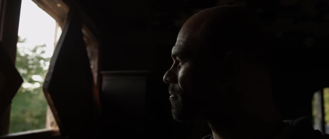 A man is standing in a dark room looking out one of the windows