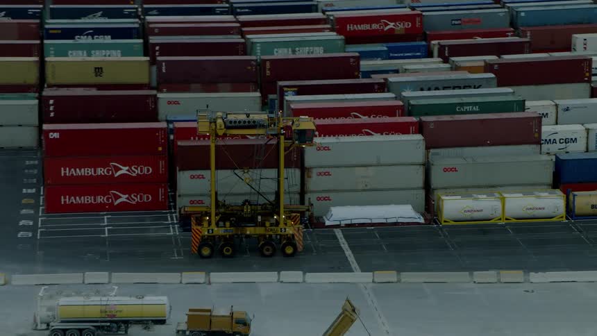 A transport vehicle travels on a dock with shipping containers
