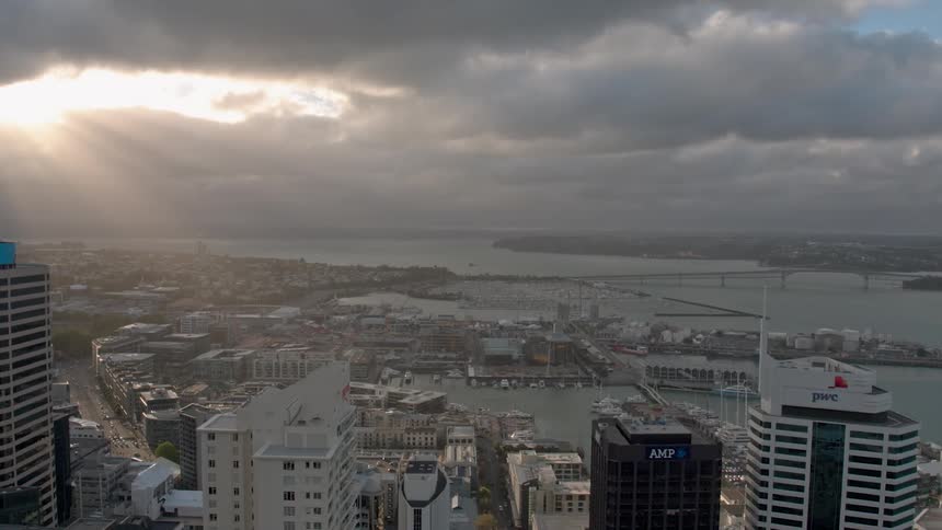 The sun shines through storm clouds hovering over a coastal city