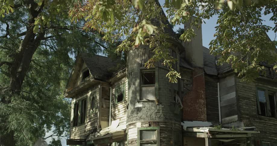 An old residential building needing renovation sits beneath a large tree in the sunshine