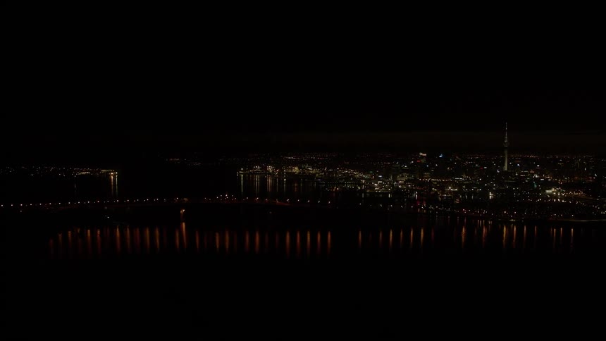 City buildings illuminate the night sky beyond a bridge