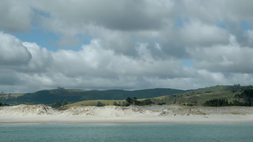 Light-colored beach on a cloudy day with green hills behind it