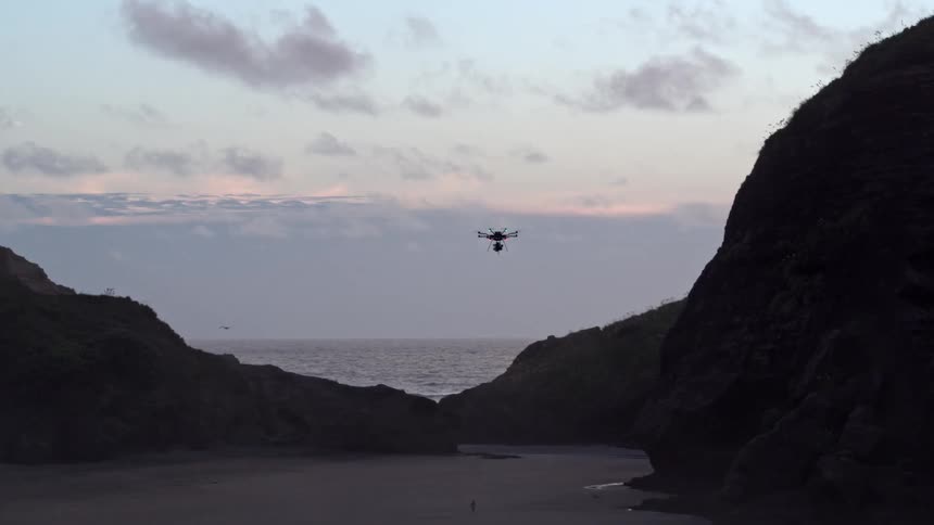 Drone flying over a beach between hills on both sides on a cloudy day