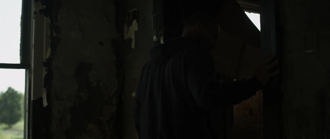 A man touches a door frame as he is walking through a run down building during the day