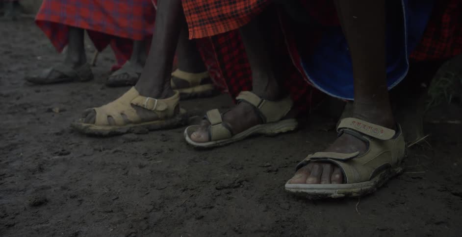 A group of maasai in sandals sit outside