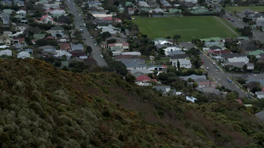 A neighborhood sprawls out in a valley beneath hills covered with trees