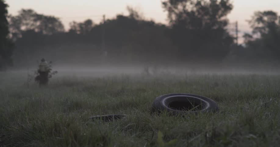 The foggy field has a tire laying in the grass