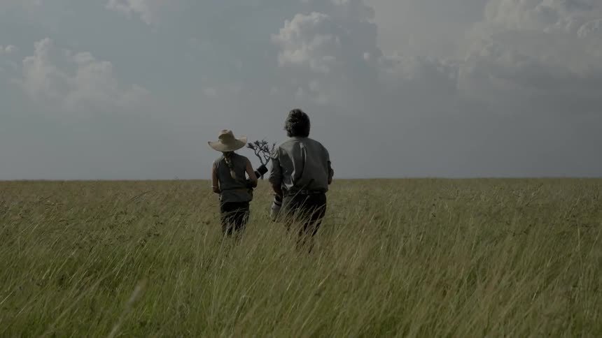 A man and woman holding cameras are walking toward a tribe of people in africa