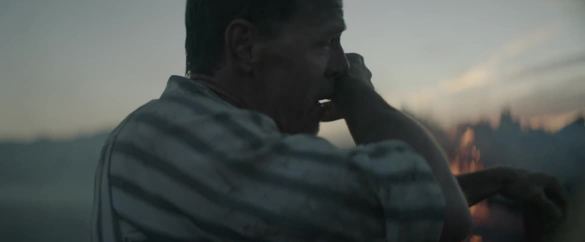 A man is breathing heaving as he watches a pile of wood burn at dusk
