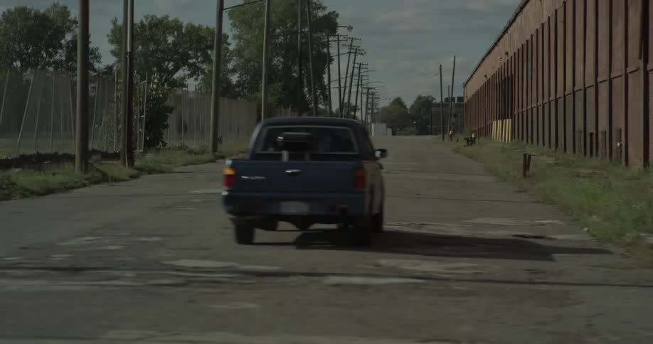 A truck travels down a tattered road with abandoned buildings