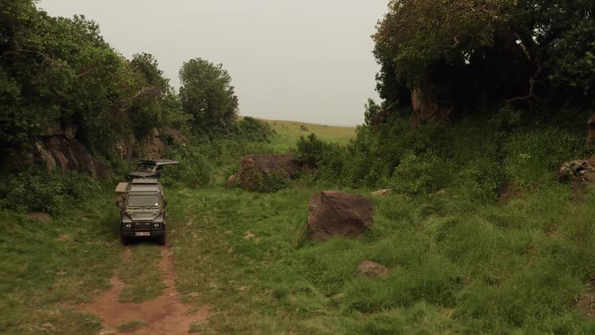 Two jeeps travel on a dirt path through a jungle gorge during the day