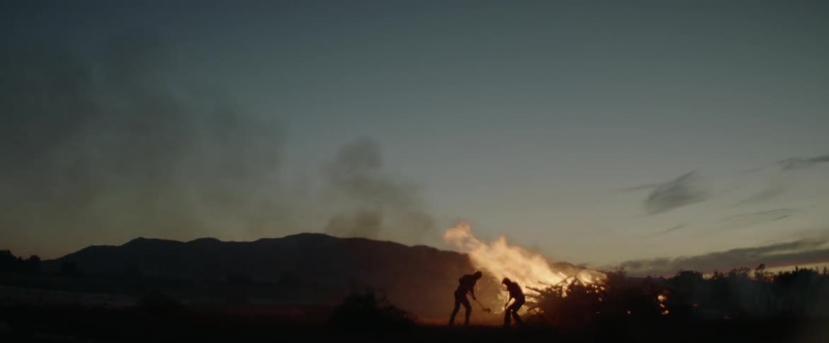 Two men are working hard to shovel dirt onto a fire at dusk