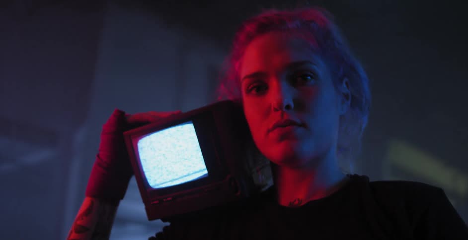 A woman is holding a television on her shoulder in a dark room