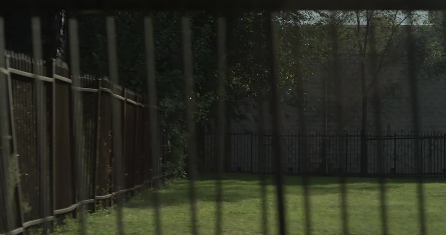 A leaning fence is outside of a lot of grass