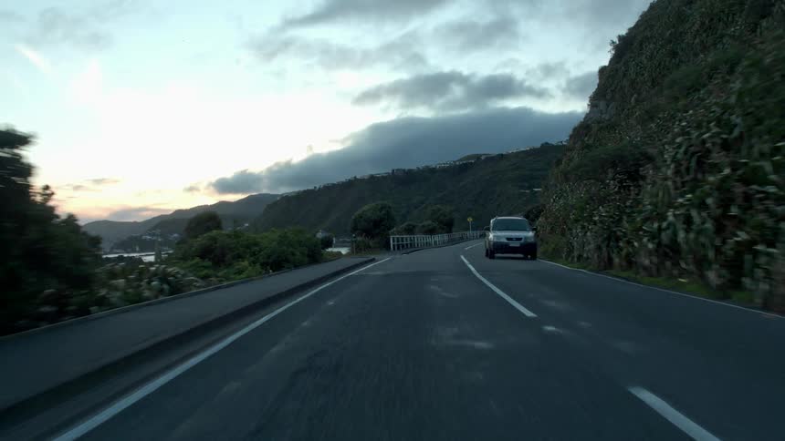 The sun shines above a shore line mountain as vehicles pass