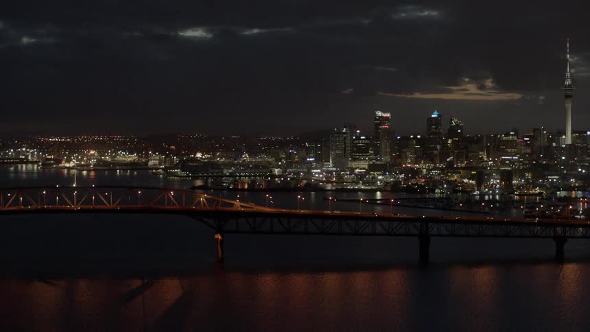 Vehicles pass along a bridge into the city at night