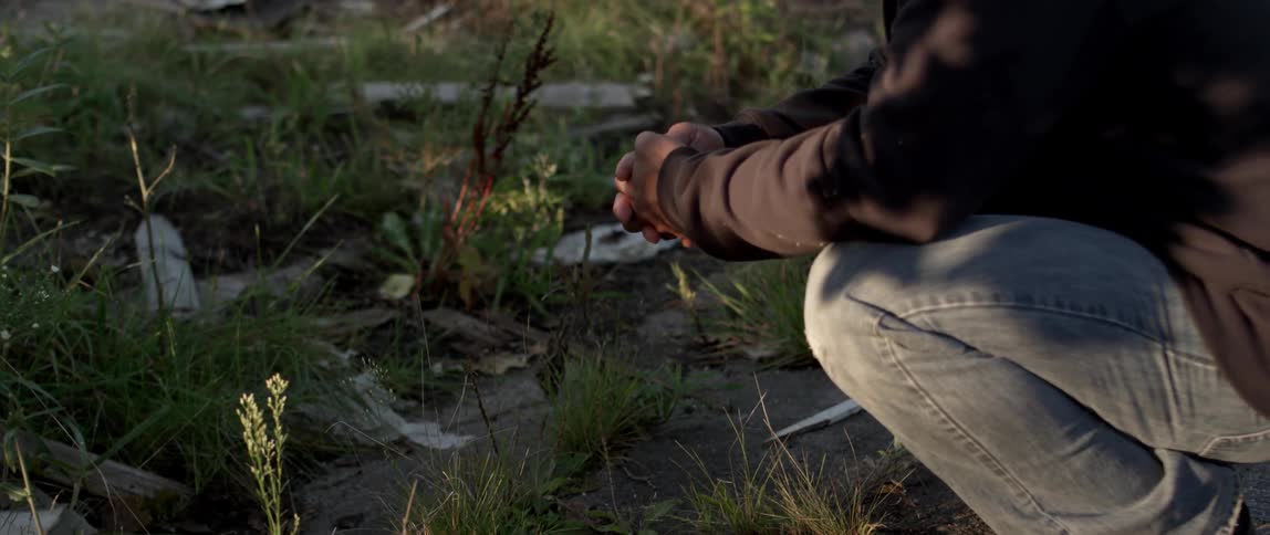 A man is crouching down by a field of green