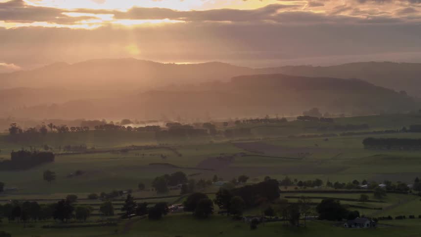 A large valley with a few trees is shown at sunset