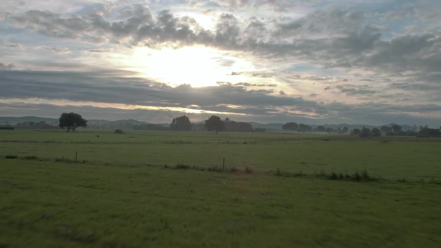 The sun is setting in the cloudy sky over the field