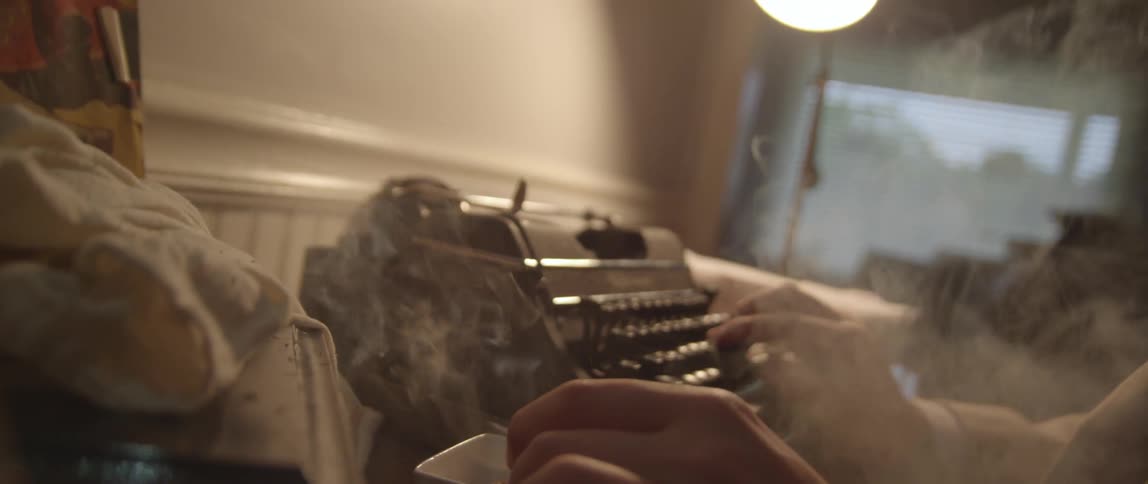 A man smokes and works at a typewriter