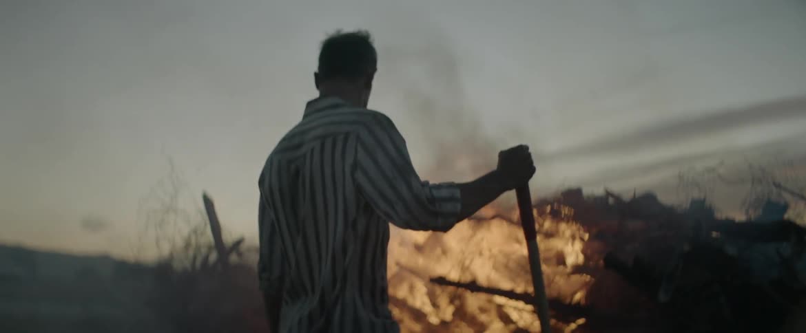 A man stands in front of a large burning fire