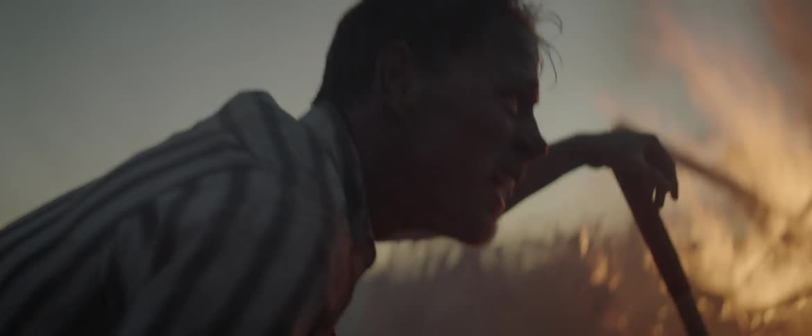 Man coughing and resting while leaning on his shovel before a burning fire outdoors