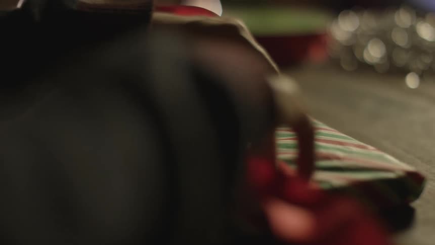 Hands are seen wrapping a bow around a christmas gift in front of a christmas tree