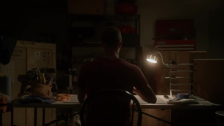A man is working at a drafting table in a garage at night