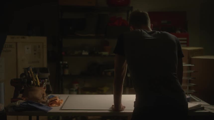A man is standing over his workbench looking at a piece of paper