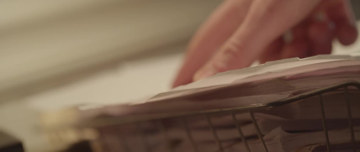 A hand is seen moving over and manipulating a sheet paper stacked in a paper tray
