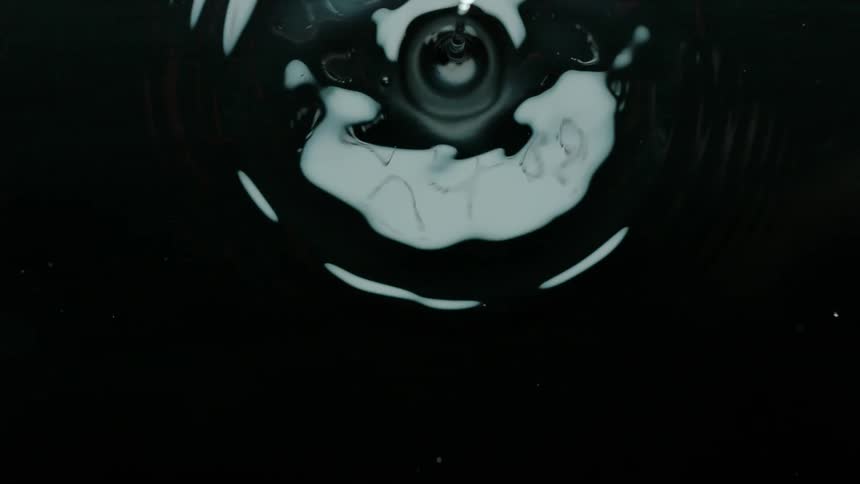 A water droplet dropping into a calm body of water creating a splash