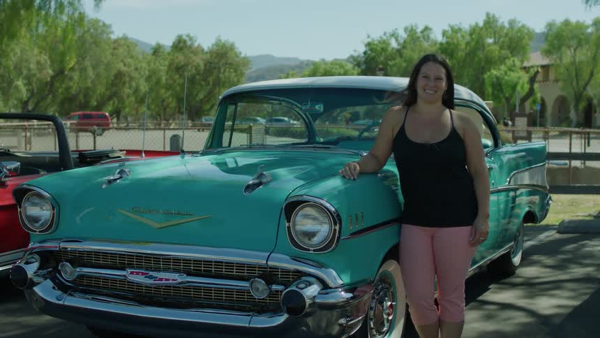 A woman leans against a teal car