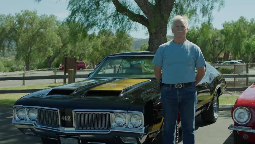 A man stands next to an old black sports car